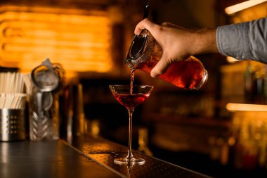 Barın üzerinde duran şarap kadehinin görüntüsünde bir erkek eli süzgeç ile karıştırıcı bardaktan su doldurur.