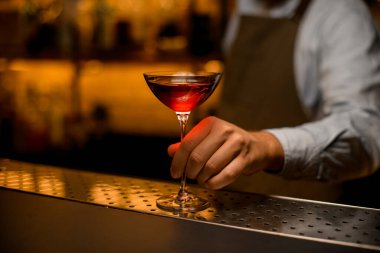 Çelik çubuk yüzeyinde içkisi olan harika bir şarap kadehi ve erkek eli tutuyor..