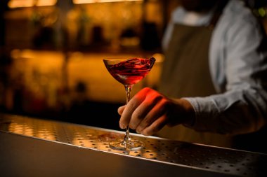 Şarap kadehinin su sıçratan manzarası çelik çubuk yüzeyinde duruyor ve erkek eli onu tutuyor..