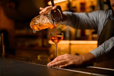 Bardağı soğuk kokteyl ve süzgeçle karıştırma manzarası. İçecekten şarap bardağına dökülüyor.