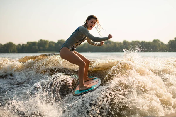 Screaming wet woman wakesurfer riding on splashing wave on a warm day — Stock Photo, Image