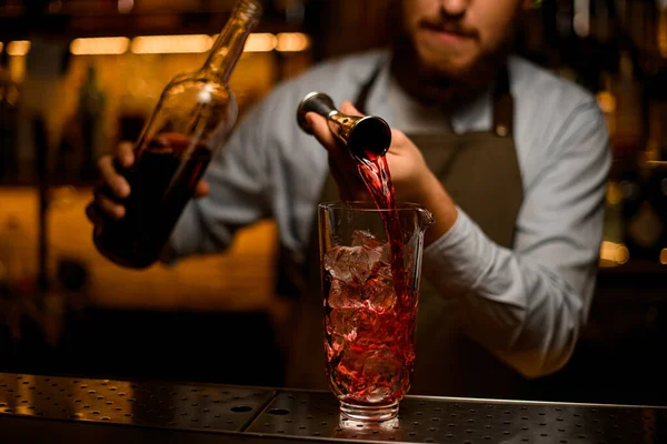 Selectieve focus op glas met ijsblokjes waarin de hand van de barman zachtjes uit een jigger drinkt — Stockfoto