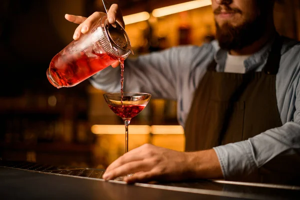 Geweldig uitzicht op het mengen van beker met ijsblokjes en een drankje met een zeef waaruit de drank wordt gegoten in een wijnglas — Stockfoto