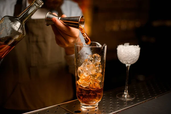 Вид стекла с кубиками льда, в который рука бармена нежно наливает напиток из кубика — стоковое фото