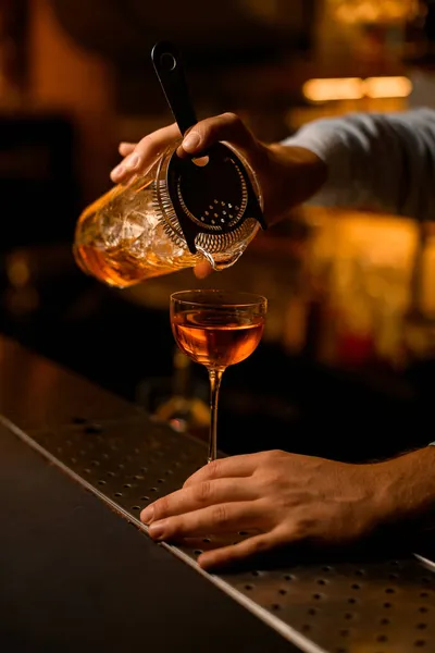 Hand van barman houdt voorzichtig een mengbeker met een zeef en giet vloeistof in wijnglas — Stockfoto