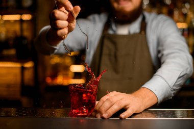 Barmenin eline buz küpü fırlattığı ve etrafa sıvı saçıldığı camın yakın görüntüsü.