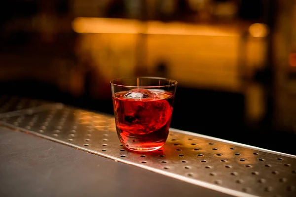 Copo transparente de coquetel com pedaço de gelo fica em um balcão de bar — Fotografia de Stock