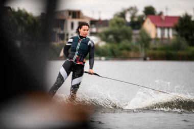 Kendine güvenen kadın wakeboardcu bir halata tutunurken wakeboard kullanıyor.