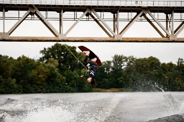 Professional woman wakeboarder holds rope and extreme jumping over water on wakeboard — Stock Photo, Image