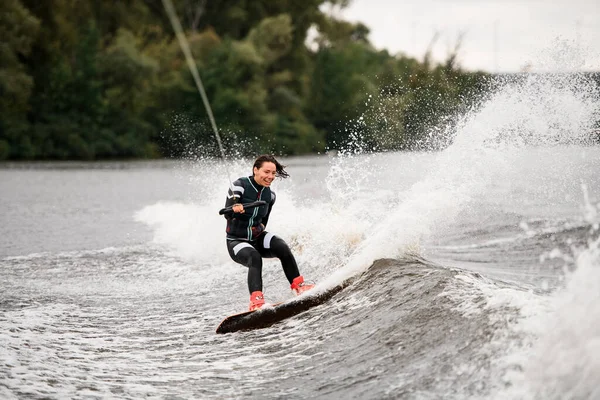 Jeune fille sportive en combinaison monte activement vagues sur wakeboard sur la rivière — Photo