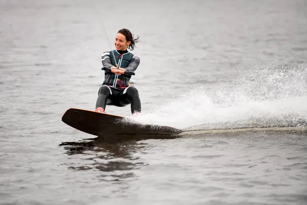 Donna felice cavalcando l'onda sul wakeboard sollevando un sacco di spruzzi al fiume — Foto Stock