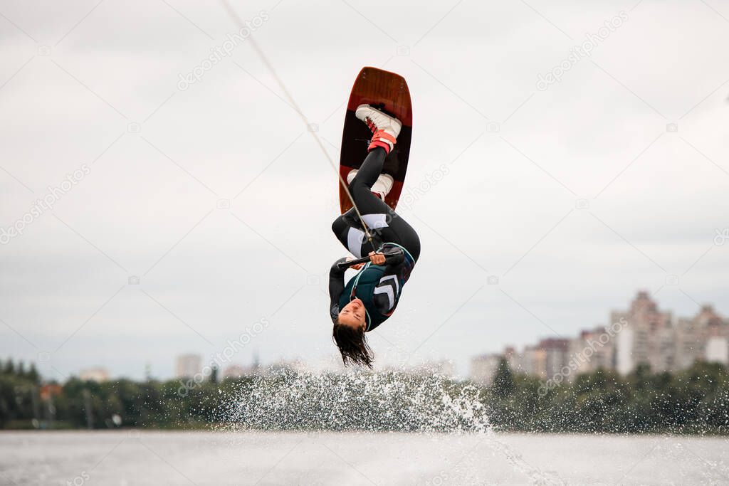 woman holds rope and doing flips and jumping over the water on wakeboarding board