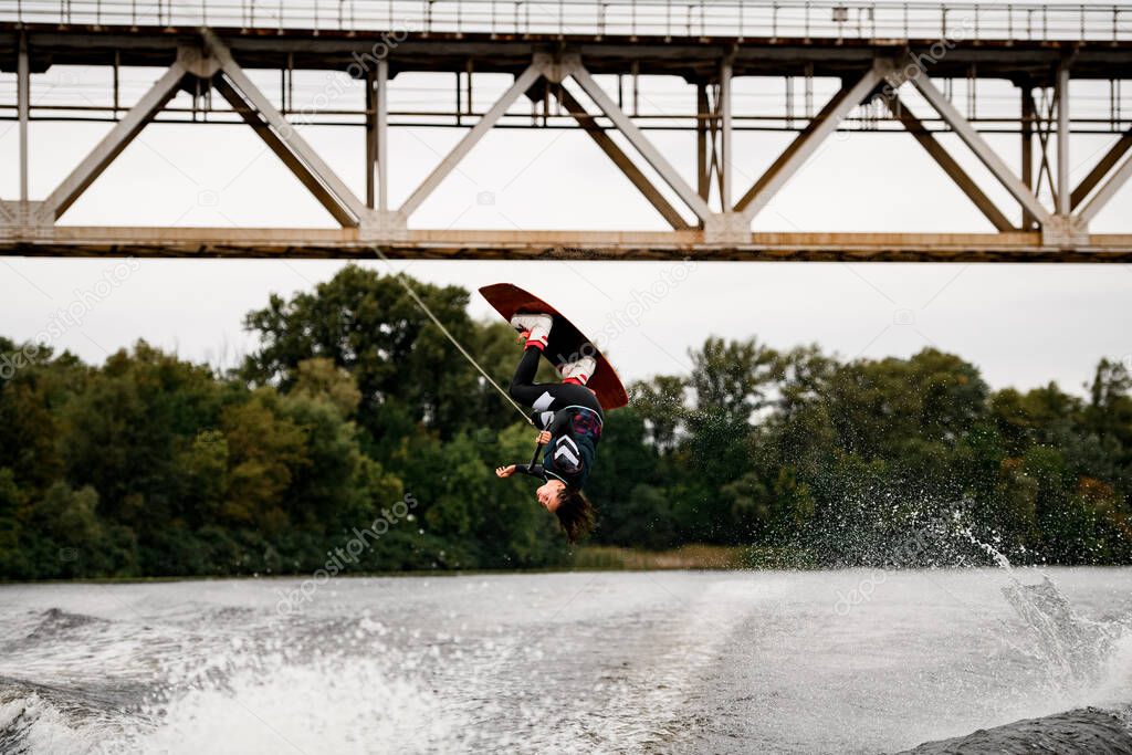 professional woman wakeboarder holds rope and extreme jumping over water on wakeboard