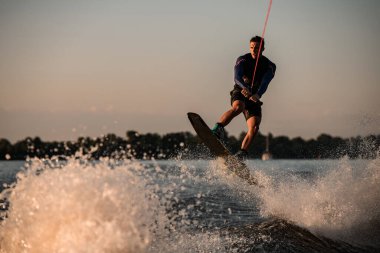 Atletik erkek wakeboardcu su sıçratan nehrin üzerinden wakeboard ile atlıyor. Yaz zamanı su sporları aktivitesi