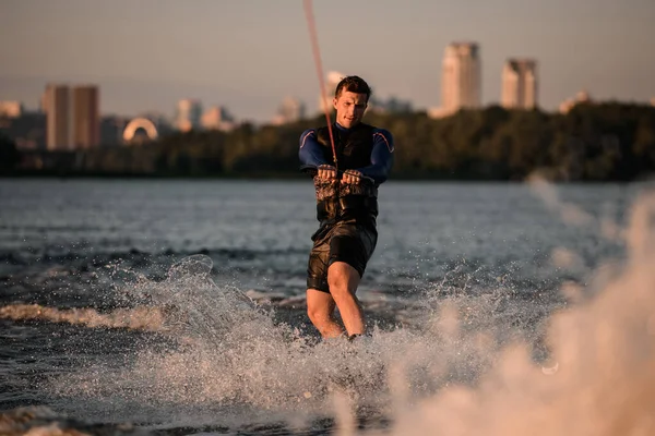 Attractive man holds rope and energetically riding wakeboard on splashing water. — Stock Photo, Image