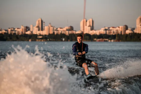 Great view of attractive man holding rope and riding wakeboard on splashing river wave. — Stock Photo, Image