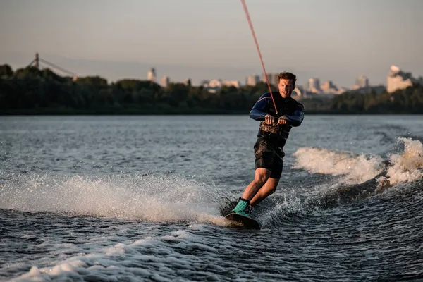 Atlétikai ember tartja kötelet és mesterien lovaglás wakeboard a fröccsenő folyó víz. — Stock Fotó