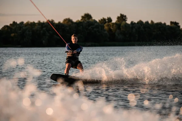 Fantastisk utsikt över attraktiv man hålla rep och energiskt ridning wakeboard på stänk flod våg. — Stockfoto