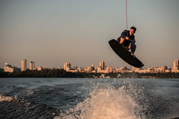 Atletisk man gör trick i hopp med wakeboard över stänk floden. Sommartid vattensporter aktivitet — Stockfoto