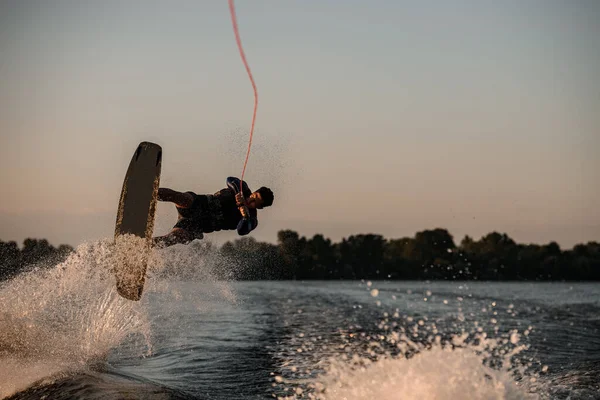 Male wakeboarder making trick in jump with wakeboard over splashing river. Summertime watersports activity — Stock Photo, Image