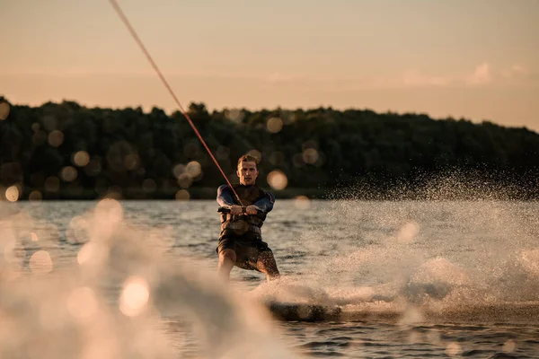 Geweldig uitzicht op aantrekkelijke man houden touw en energiek rijden wakeboard op spetterende rivier golf. — Stockfoto