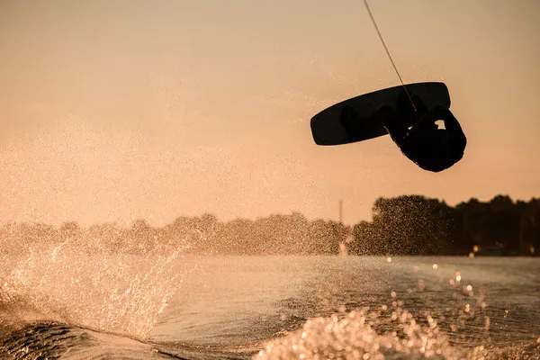 Wonderful silhouette of male rider holding rope and making extreme jump on wakeboard over splashing water. — Stock Photo, Image