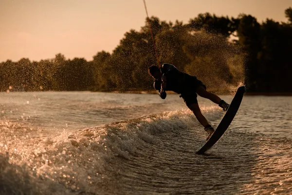 Grande vista do homem fazendo truque e saltar com wakeboard na superfície de água salpicando. — Fotografia de Stock