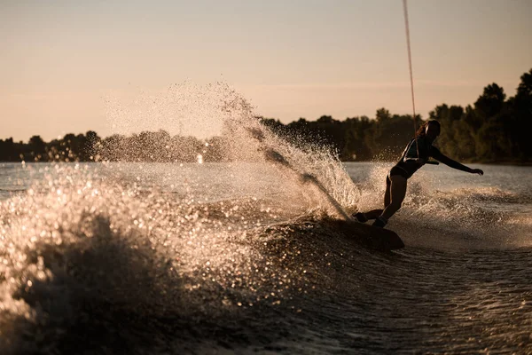 ロープを持っている女性のシルエットの素晴らしい景色と巧みに水しぶき波にウェイクボード上に乗る. — ストック写真