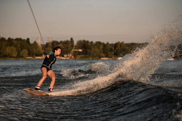 Vista de mujer guapo sosteniendo la cuerda y paseos por la ola en wakeboard —  Fotos de Stock