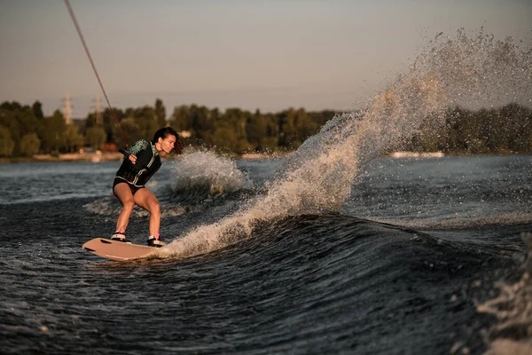 Vista de mujer atractiva sosteniendo la cuerda y cabalga por la ola en wakeboard —  Fotos de Stock