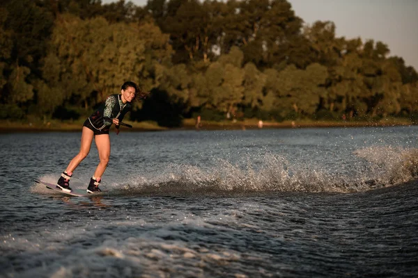 Vue de la femme heureuse tient la corde et magistralement équitation wakeboard sur éclaboussant l'eau de la rivière. — Photo