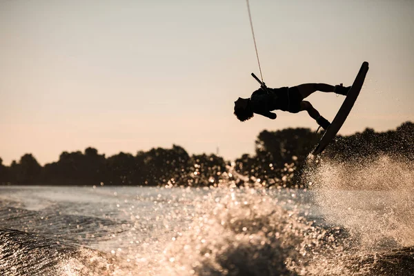 Vacker silhuett av kvinnliga ryttare hålla rep och göra hoppa på wakeboard vid solnedgången. Vattensporter. — Stockfoto