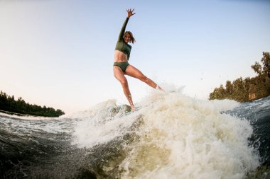 Gülümseyen atletik kadın nehir dalgası üzerinde dengede duruyor.