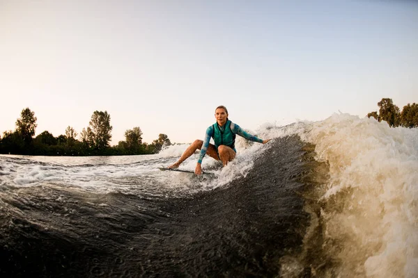 Belle femme assise sur le surf et monte la vague et touche la vague d'une main — Photo