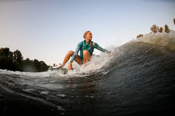 Vonzó nő ül a szörfözés és lovagol a hullám, és megérinti a hullám egy kézzel — Stock Fotó
