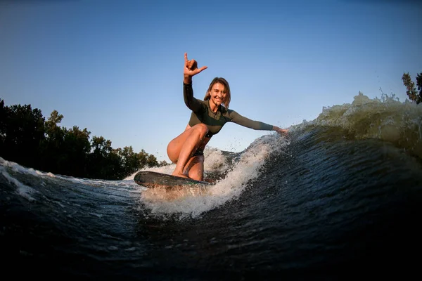 Mujer alegre se sienta en paseos de surf y toca las olas con una mano y mostrar gesto de la mano —  Fotos de Stock