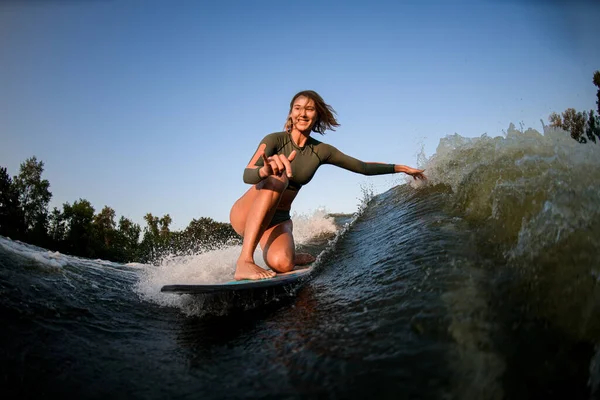 Mulher sorrindo senta-se em passeios de surf e toca ondas com uma mão e mostrar gesto mão — Fotografia de Stock