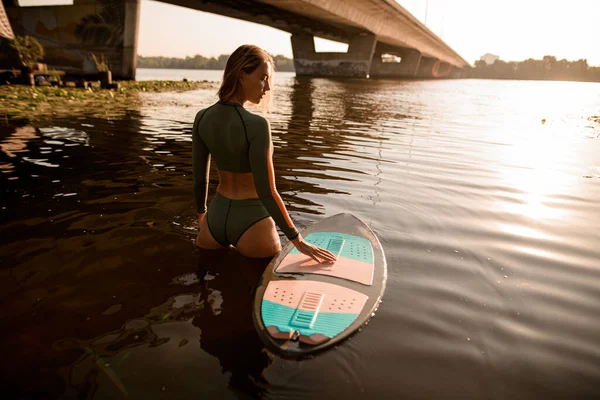 Suda güzel bir kadının, yanında bir sörf tahtasıyla dikiz manzarası. — Stok fotoğraf