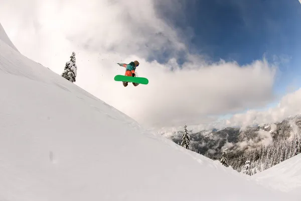 Snowboarder executa salto magistral no ar sobre encosta de montanha nevada — Fotografia de Stock