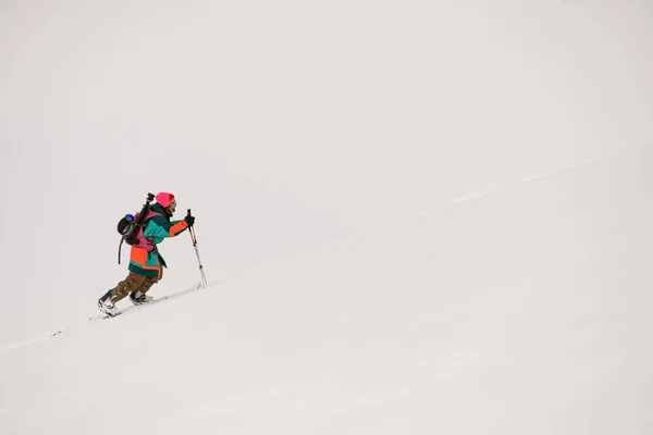 Лыжник в ярком лыжном костюме взбирается на снежную гору. — стоковое фото