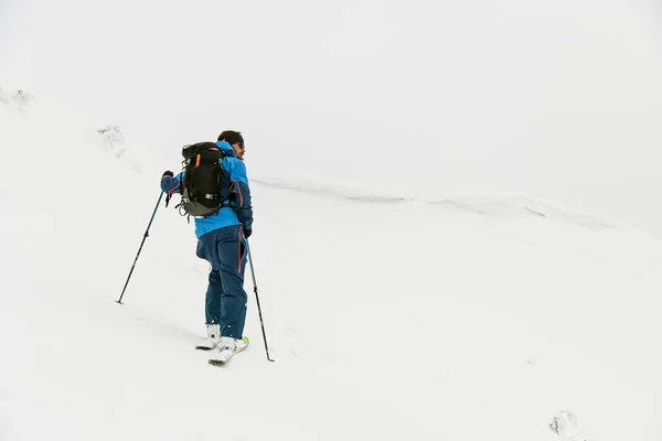 Hátsó kilátás ember síelő trekking pólusok havas dombon felhős ég a háttérben. — Stock Fotó