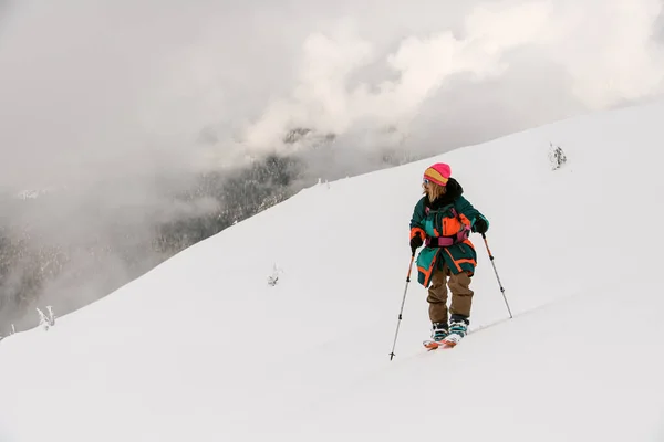 Skifahrer mit Trekkingstöcken auf schneebedecktem Hügelweg mit wolkenverhangenem Himmel im Hintergrund. — Stockfoto