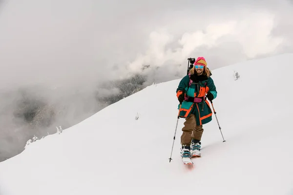 Vista frontale dell'uomo sciatore sorridente che cammina lungo il sentiero collinare innevato — Foto Stock