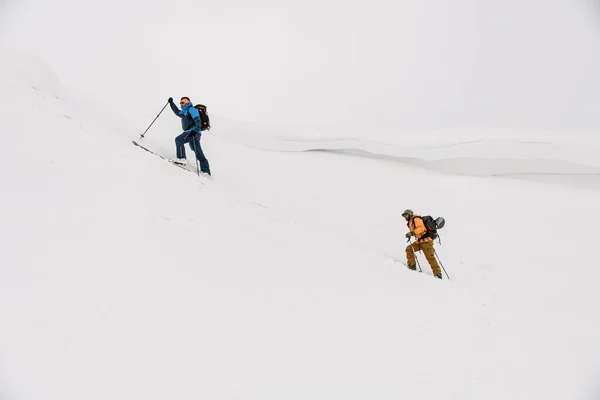 İki erkek kayakçı kar kaplı bir dağa tırmanır beyaz karla kaplı bir zemine. — Stok fotoğraf