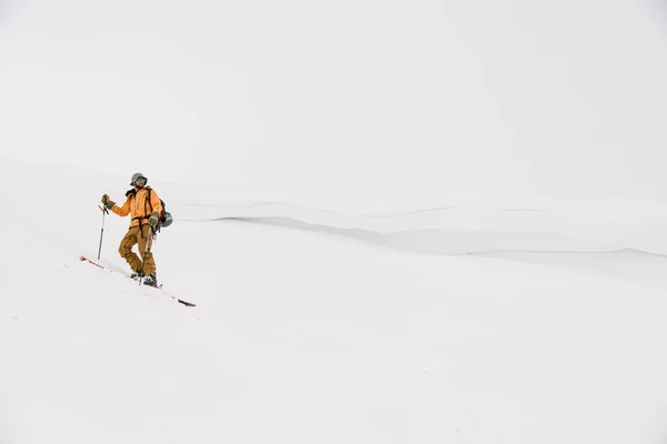 Человек лыжник в желтом костюме стоит и смотрит в сторону на фоне белого снега — стоковое фото