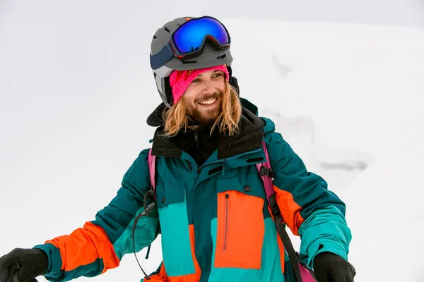 Χαρούμενη χαμογελαστός σκιέρ άνθρωπος σε φωτεινό πολύχρωμο κοστούμι σκι με φόντο το χιόνι — Φωτογραφία Αρχείου