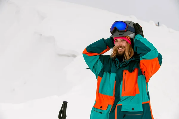 Χαμογελαστός άνθρωπος σκιέρ σε φωτεινό πολύχρωμο κοστούμι σκι με φόντο το χιόνι — Φωτογραφία Αρχείου