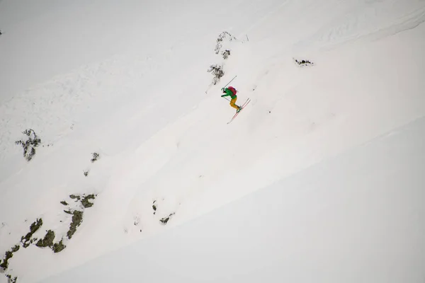 Sidovy av en skidåkare hoppa och glida ner lutning mot bakgrund av snö — Stockfoto