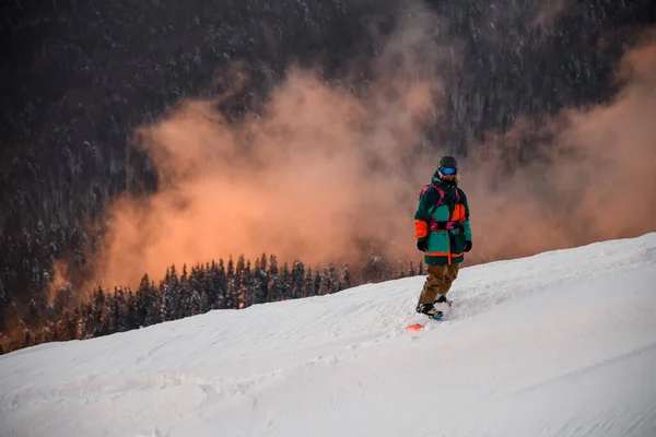 Atleta em estandes de traje de esqui em snowboard na encosta da montanha coberta de neve — Fotografia de Stock