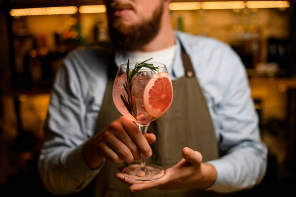 Enfoque selectivo en vidrio de copa con bebida fría con rodaja de pomelo y romero en manos de cantinero masculino — Foto de Stock